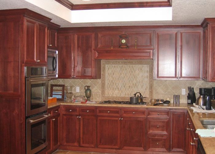 Warm kitchen with rich cherry wood cabinets, adorned with a vintage clock and decorative items. Modern appliances and neutral tile backsplash complete the cozy ambiance.