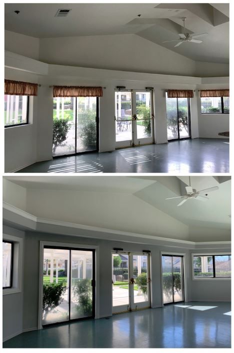 Large, bright room with vaulted ceiling and ceiling fans. Floor-to-ceiling windows and sliding doors showcase an outdoor garden, creating a welcoming, airy space.