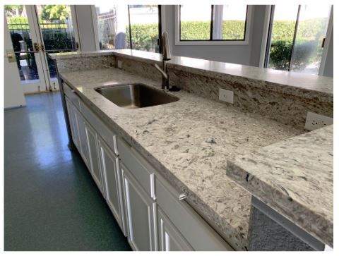 Spacious kitchen with speckled granite countertop, stainless steel sink, and white cabinets. Natural light from large windows creates an airy feel.