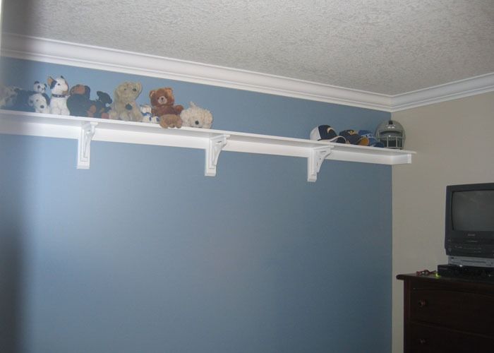 A row of plush toys and hats are neatly arranged on a white shelf against a two-tone blue and beige wall. Below, a vintage TV sits on a dark wooden dresser.