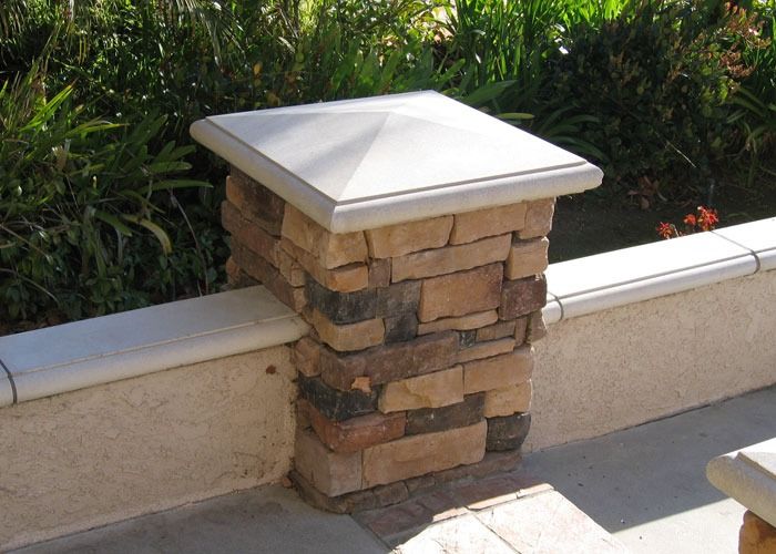 Stone pillar with a square cap, part of a low wall, set against lush greenery. The sunlit scene conveys a warm, inviting outdoor space.