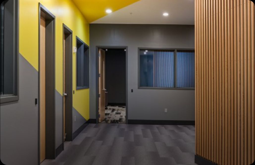 A modern hallway with bold contrasts. The left wall is yellow and gray with three doors. The right features wooden slats. Gray carpet adds a sleek touch.